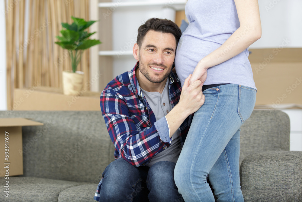 happy young man putting ear to pregnant womans belly happy young man putting ear to pregnant womans belly