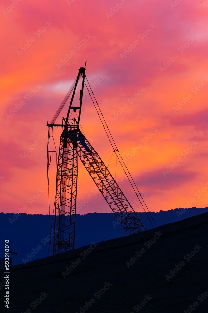 Vertical shot of a silhouette of an industrial crane in front of the sunset sky