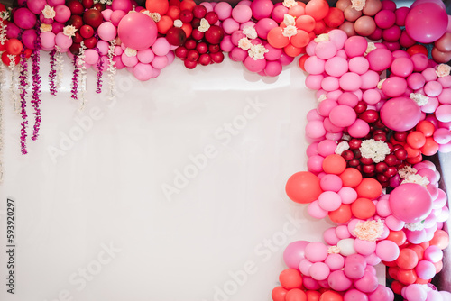 Arch with balloons, party decor. White photo wall decoration space or place with pink, red, maroon, and burgundy balloons. Trendy spring decor. Celebration concept. Birthday party. Wedding reception.