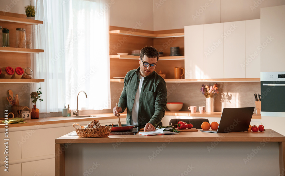 Checking the receipt while preparing the food. Handsome man is on the kitchen at daytime Checking the receipt while preparing the food. Handsome man is on the kitchen at daytime