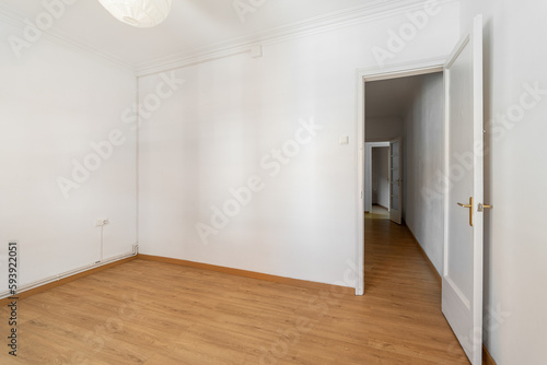 An empty small bright room with white walls and an open door overlooking a corridor in a spacious house. The concept of a room in a hotel or moving. Copyspace