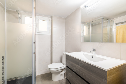 Comfortable white toilet with a large sink  a mirror  a toilet bowl and a glazed shower in a new comfortable hotel. The concept of a simple but stylish bathroom design