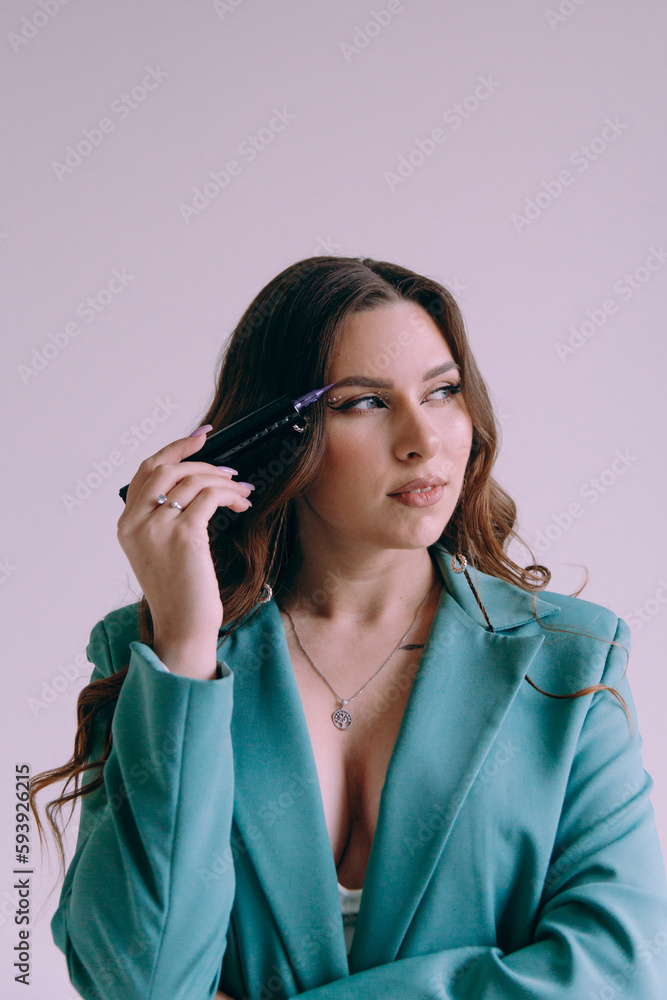 Luxurious girl with beautiful makeup and hairstyle, permanent makeup specialist, holds tools in her hands. Photoshoot in a photo studio in a suit, jeans and a shirt.