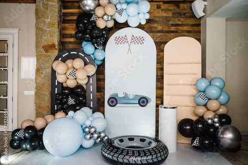 Birthday decorations with blue, brown, black, silver balloons for party. Arch for a celebration event. Photo wall decoration space or place for text. Trendy decor with flag, race, wheel, car for boy.