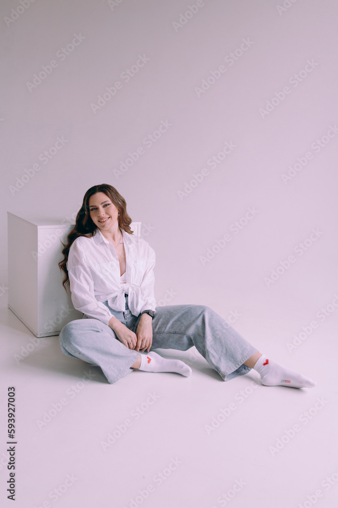 Luxurious girl with beautiful makeup and hairstyle, permanent makeup specialist, holds tools in her hands. Photoshoot in a photo studio in a suit, jeans and a shirt.