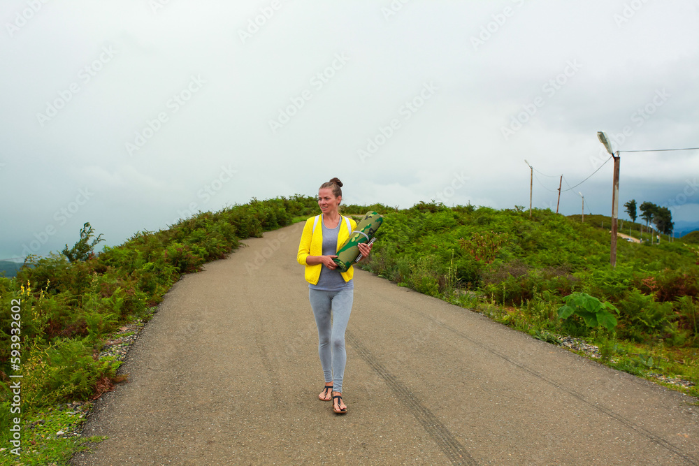 Young woman hiker with backpack walking on a mountain road in summer