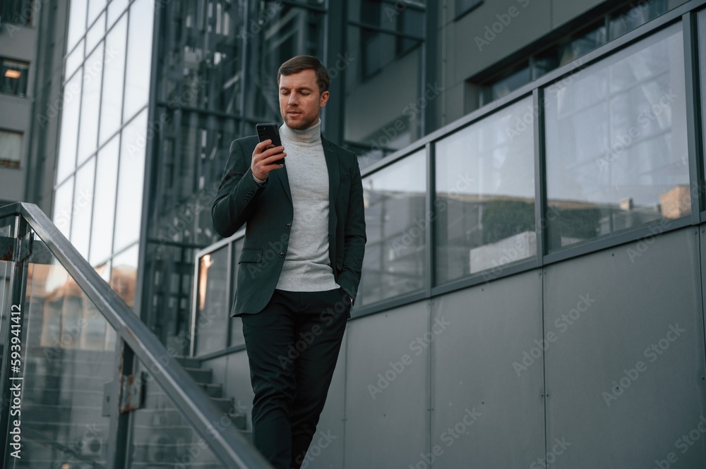 Using social media by smartphone. Handsome man in formal clothes is outdoor near the business building Using social media by smartphone. Handsome man in formal clothes is outdoor near the business building