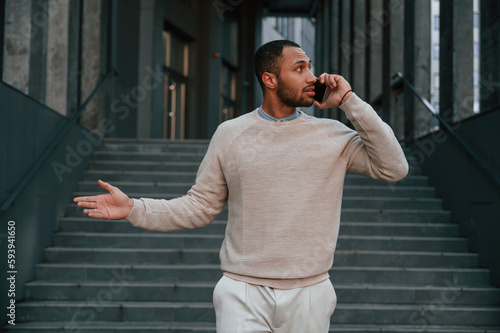 Having a phone call. Handsome black man is outdoors near the business building © standret