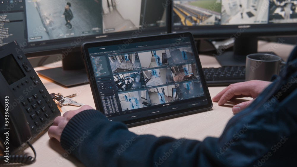 Security operator controls CCTV cameras in office, uses digital tablet and computers with surveillance camera playback on screens. High tech security with facial recognition. Concept of social safety. Security operator controls CCTV cameras in office, uses digital tablet and computers with surveillance camera playback on screens. High tech security with facial recognition. Concept of social safety.