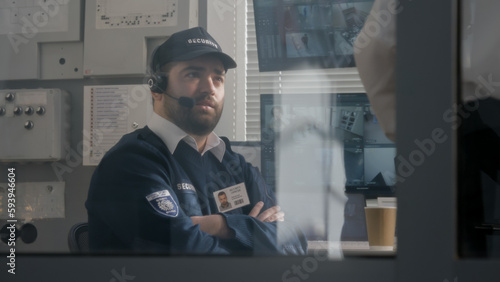 Security officer in headset talks with colleague. Men work in surveillance room. View from security cameras displayed at computer monitors. Observation and CCTV technology. Concept of social safety.