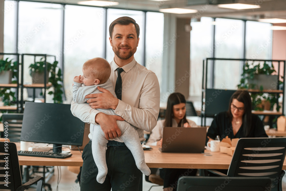 Infant baby is in the office where group of people are working together