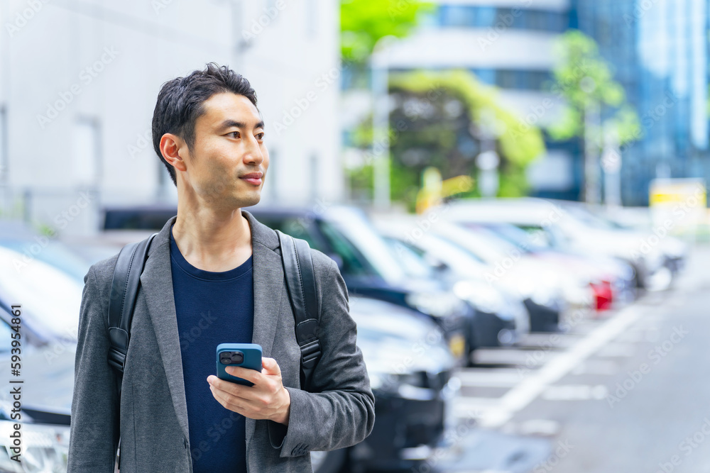 スマホを持って駐車場に立つ男性 スマホを持って駐車場に立つ男性