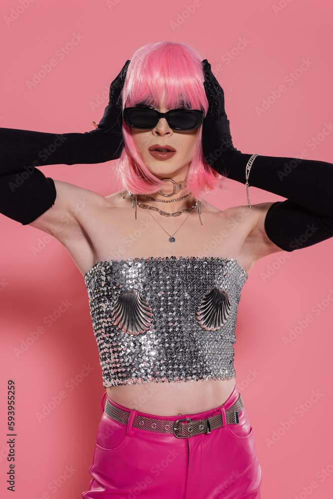 Trendy drag queen in sunglasses and gloves touching wig on pink background. Trendy drag queen in sunglasses and gloves touching wig on pink background.