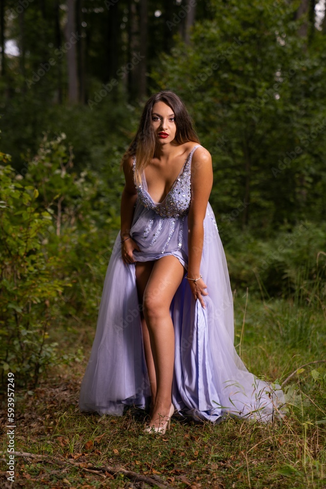 Vertical shot of the pretty woman wearing a long purple dress and standing in the woods
