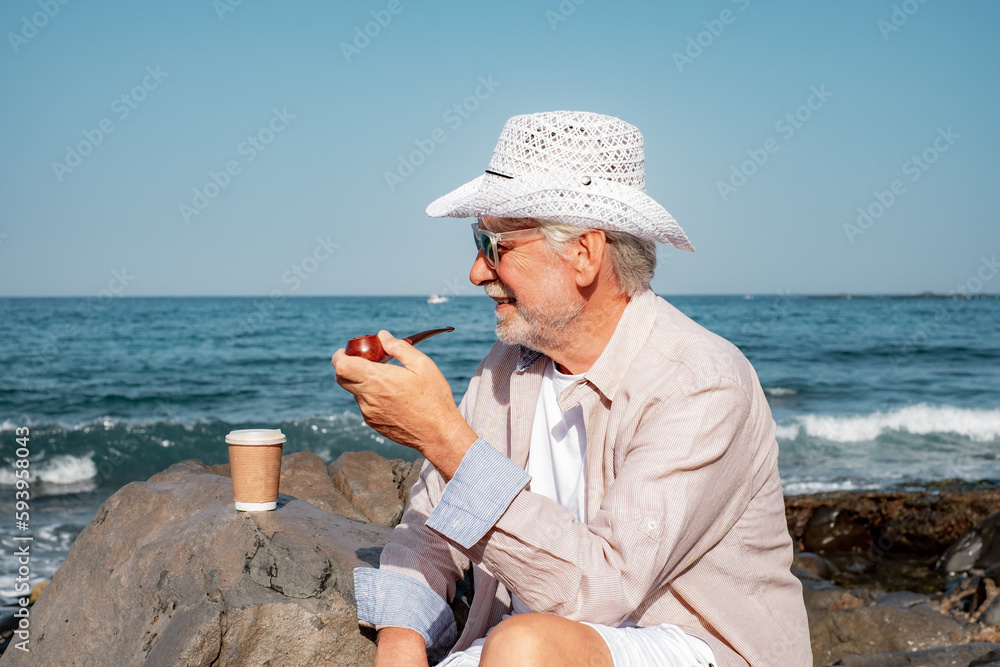 Vacation Retirement Lifestyle at Sea, Senior Man Sitting Relaxing at Beach Smoking Pipe - Stilish Elderly Grandfather with White Hat Enjoying Free time
