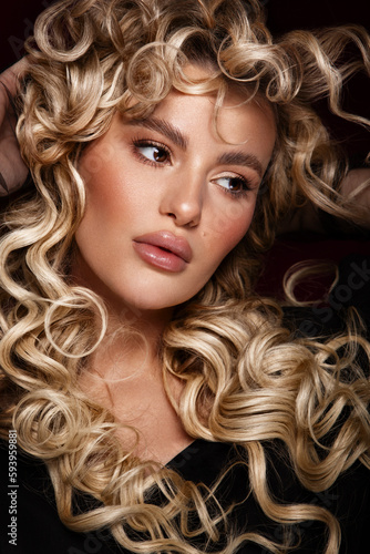 Blondie girl with long and shiny curly hair . Beautiful model woman with wavy hairstyle