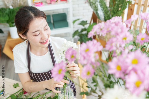 Attractive Asian Korean Woman florist in apron arranging flowers while working at flower shop.