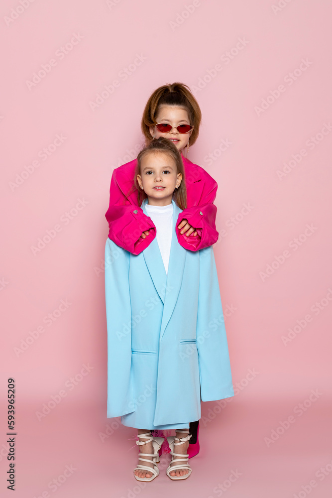Two little girls dressed like adults. Children wearing oversized clothes. fashionable kids. Isolated on pink background. Two little girls dressed like adults. Children wearing oversized clothes. fashionable kids. Isolated on pink background.