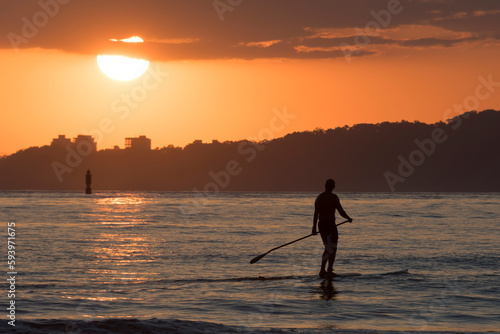Silhouette of man practicing stand up paddle in the bay of santos city at sunset.