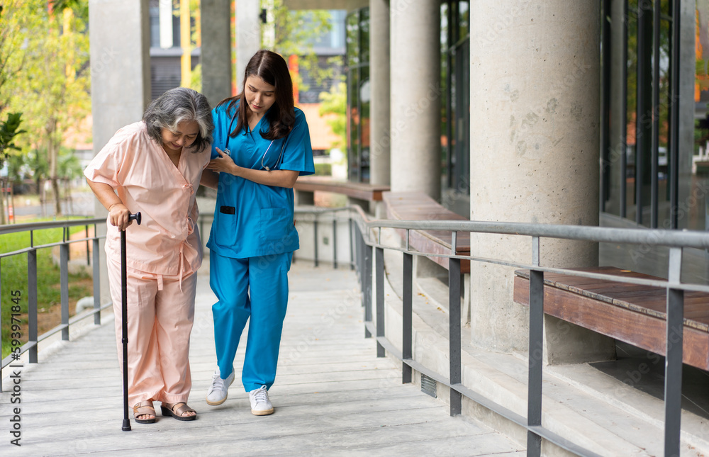 Asian careful caregiver or nurse hold patient hand and encourage patient, walking in garden. Concept of happy retirement with care from a caregiver and Savings and senior health insurance.