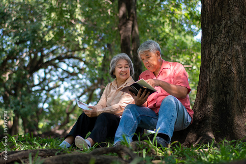 Happy Asian old senior couple with gray hair reading a book outside in park. Concept of happy elderly after retirement and good health