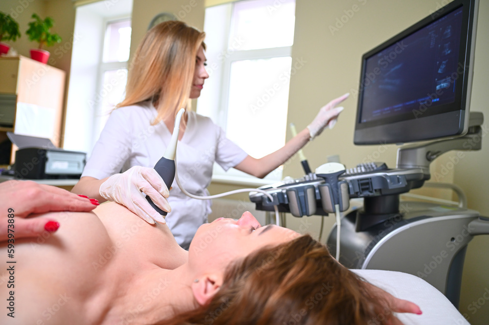 Fototapeta premium Professional female gynecologist performs an examination of the mammary glands using ultrasound scanner. Breast ultrasound examination. Prevention breast cancer. Screening after plastic surgery.