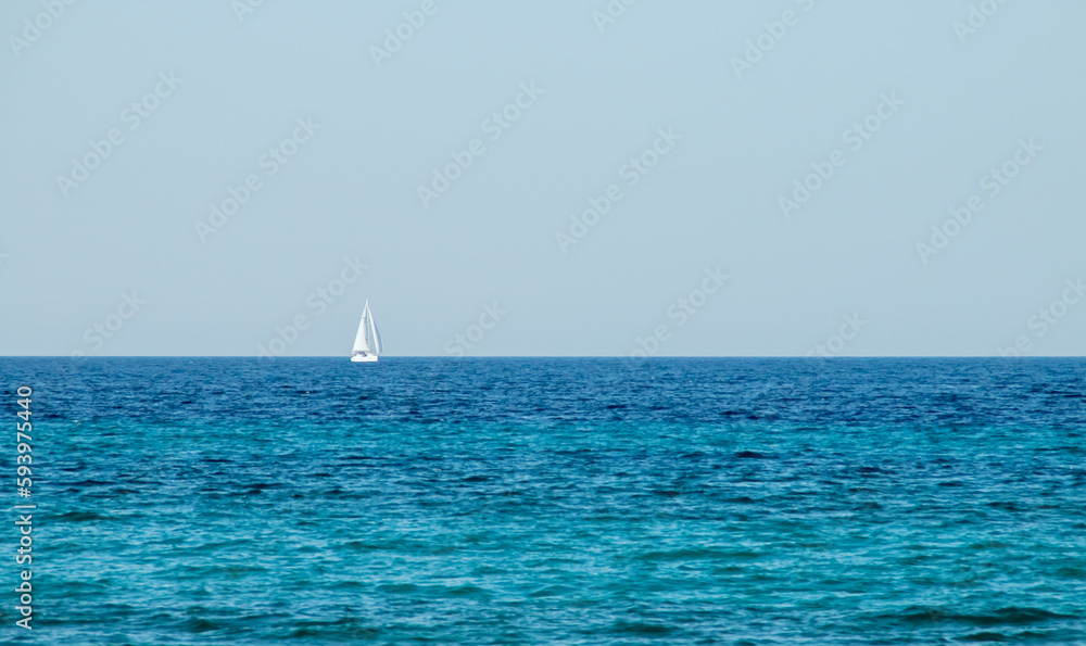 Velero navegando en el horizonte sobre un mar de aguas turquesas. Otranto, Italia. Velero en ruta por el canal de Otranto que conecta el mar Jónico y el mar Adriático.