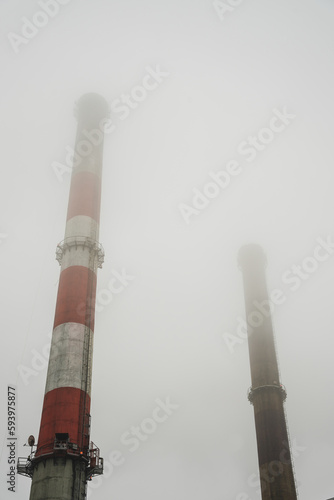 Smog w mieście, wysokie kominy przemysłowe w gęstej mgle. 