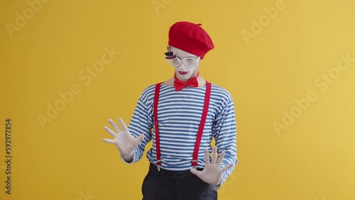 A young mime guy looking for weaknesses, voids in the wall. Portrait of a mime playing a funny performance, standing on a yellow background photo