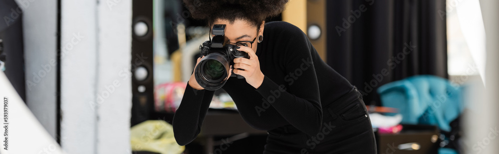 african american content producer in black turtleneck photographing on digital camera in photo studio, banner.