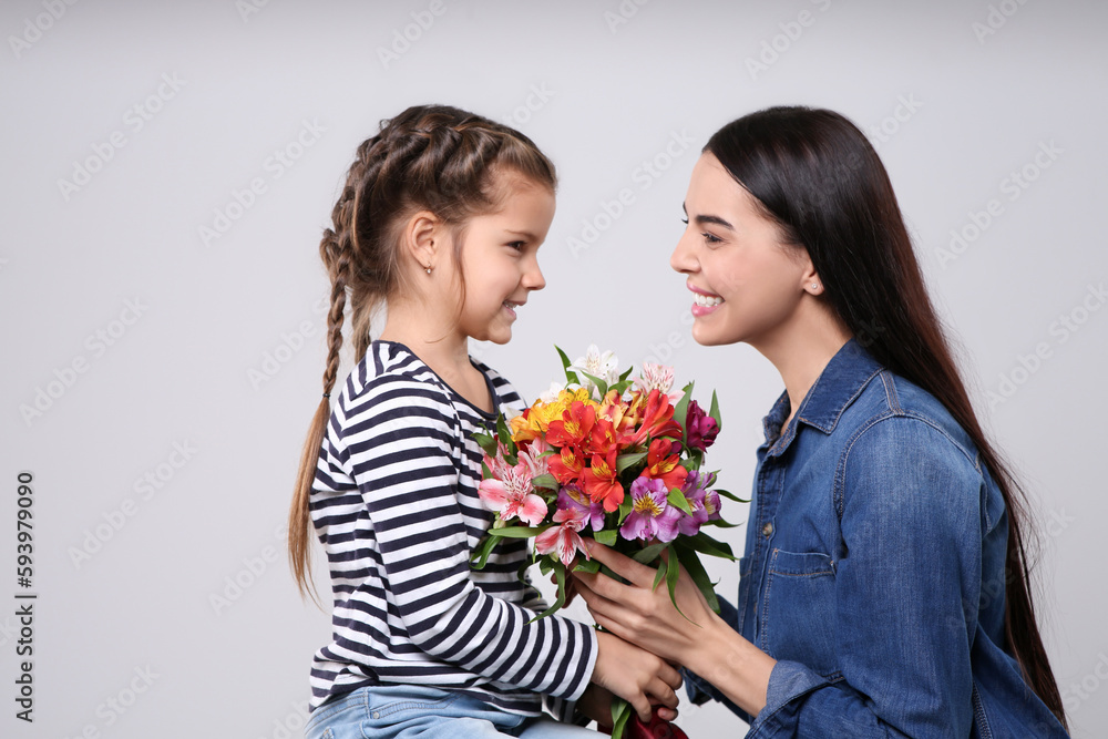 Happy woman with her cute daughter and bouquet of beautiful flowers on light grey background. Mother's day celebration Happy woman with her cute daughter and bouquet of beautiful flowers on light grey background. Mother's day celebration