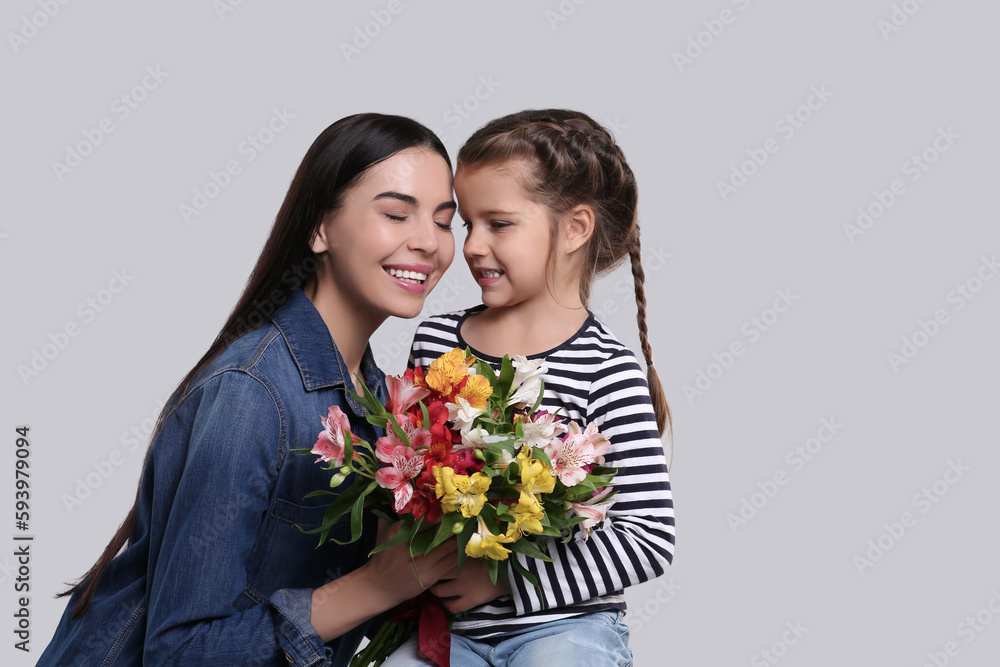 Happy woman with her cute daughter and bouquet of beautiful flowers on light grey background. Mother's day celebration Happy woman with her cute daughter and bouquet of beautiful flowers on light grey background. Mother's day celebration