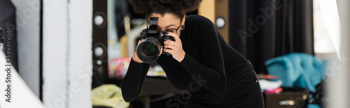 african american content producer in black turtleneck photographing on digital camera in photo studio, banner. © LIGHTFIELD STUDIOS