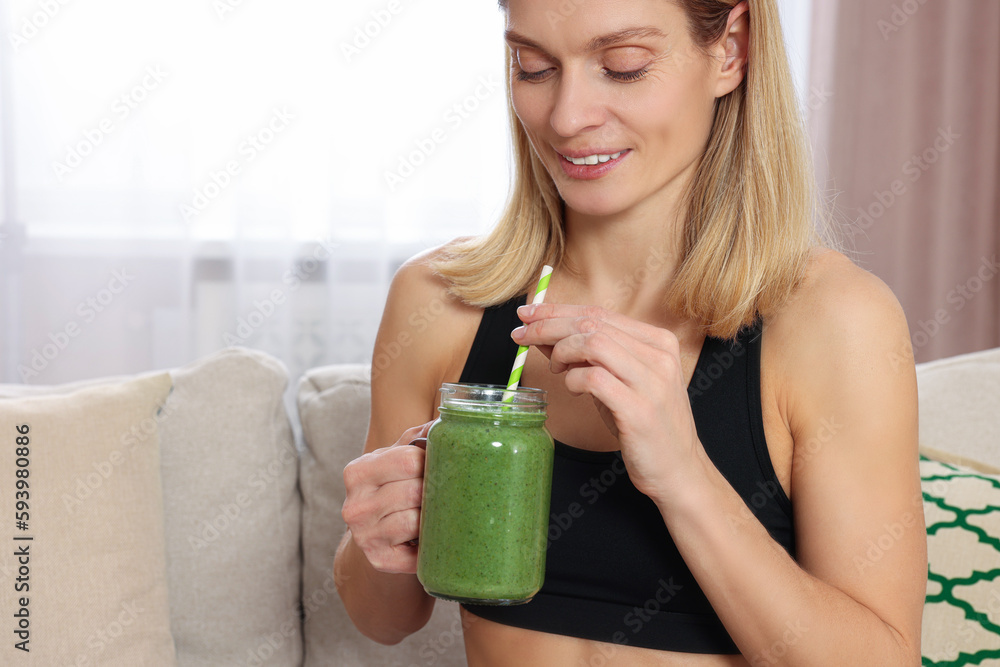Young woman in sportswear with glass mason jar of fresh smoothie at home, closeup. Space for text Young woman in sportswear with glass mason jar of fresh smoothie at home, closeup. Space for text