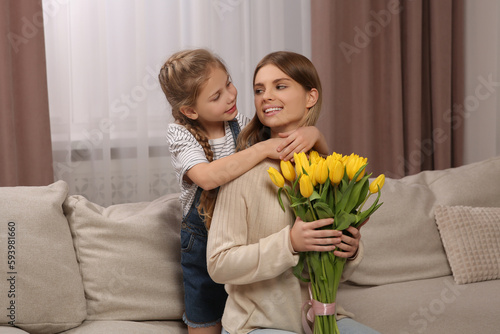 Little daughter congratulating mom with bouquet of yellow tulips at home. Happy Mother's Day