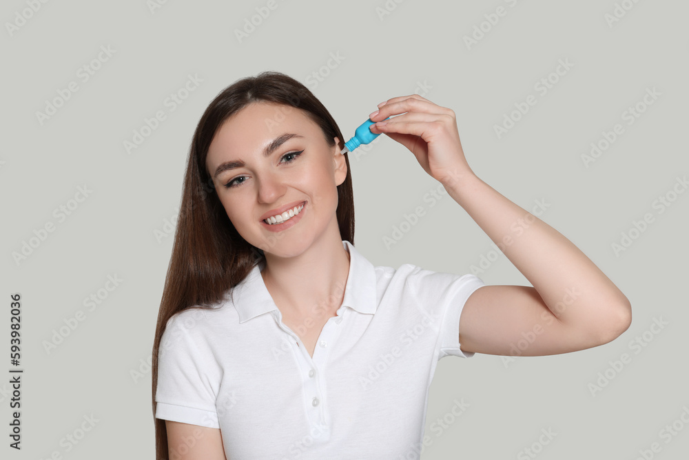 Young woman using ear drops on light grey background Young woman using ear drops on light grey background