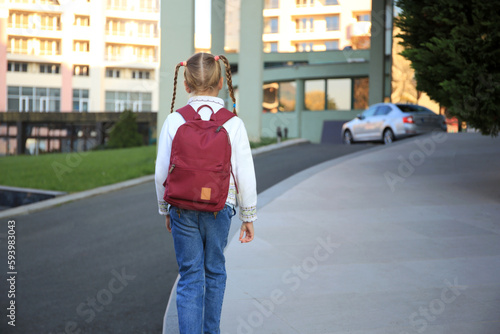 Cute little girl with backpack on city street back view. Space for text