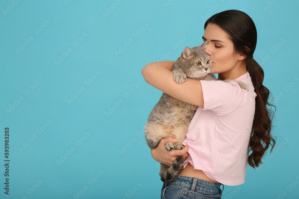 Young woman kissing her adorable cat on light blue background, space for text Young woman kissing her adorable cat on light blue background, space for text