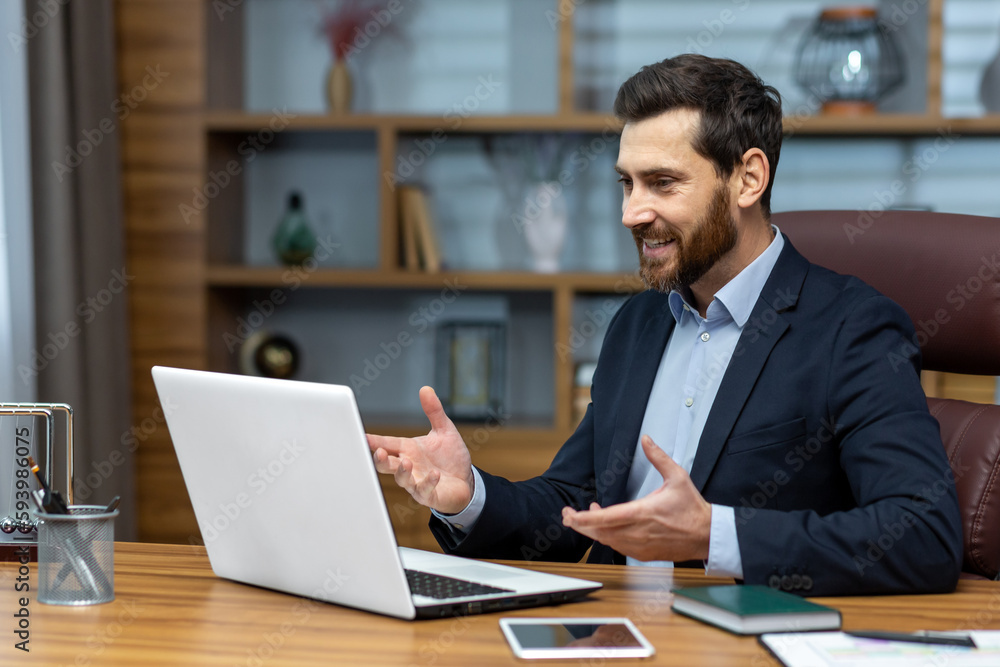 Successful smiling boss talking on video call, man in business suit inside office using laptop for online meeting, businessman joyfully talking and reporting. Successful smiling boss talking on video call, man in business suit inside office using laptop for online meeting, businessman joyfully talking and reporting.