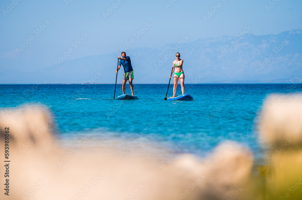 Couple riding SUP stand up paddle on vacation.