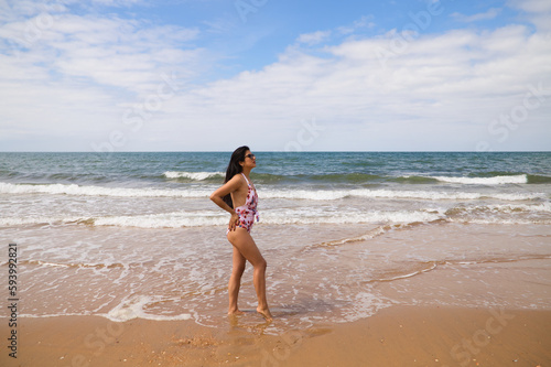 Beautiful and young latin woman is walking along the shore of the beach and posing for photos. Beautiful woman is on holiday on a paradise beach. Holiday and travel concept.