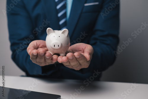 Close up view of young businessman holding piggy bank in the office room. Money investment concept.