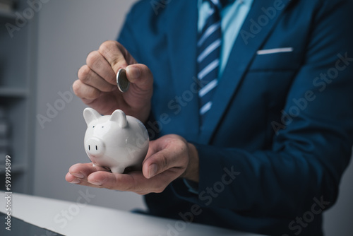 Close up view of young businessman depositing money in piggy bank in the office room Fototapeta