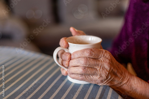 hands of an old woman hold a white mug with tea