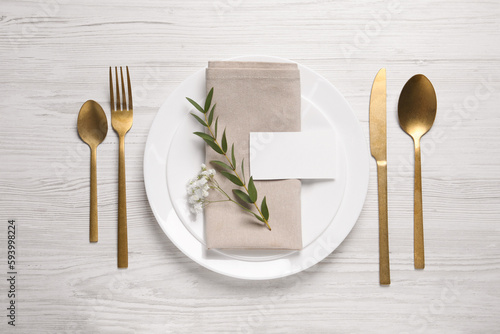 Stylish setting with cutlery, eucalyptus leaves and blank card on white wooden table, flat lay. Space for text
