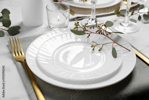 Stylish setting with cutlery and eucalyptus leaves on white marble table, closeup