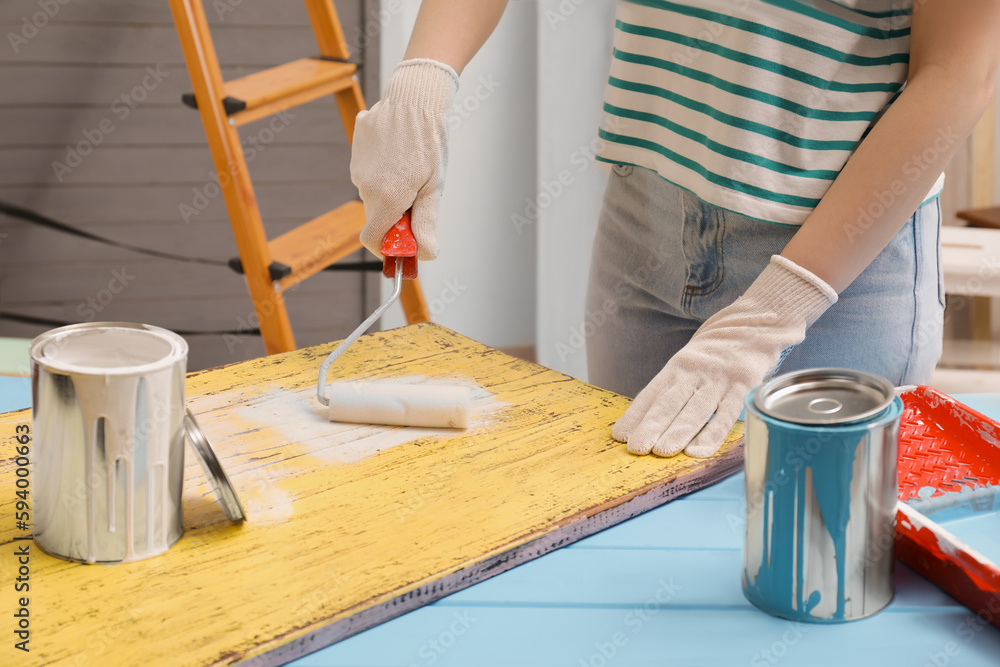 Woman using roller to paint plank with white dye at light blue wooden table indoors, closeup Woman using roller to paint plank with white dye at light blue wooden table indoors, closeup