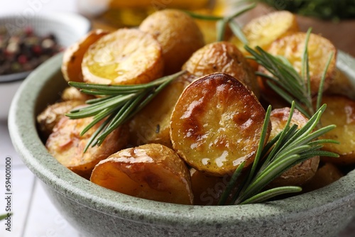 Tasty baked potato and aromatic rosemary in bowl on table, closeup