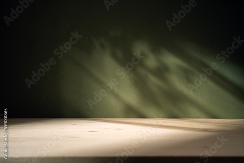 Empty table on khaki green texture wall background. Composition with leaves shadows on the wall and light reflections. Mock up for presentation, branding products, cosmetics food or jewelry.	
