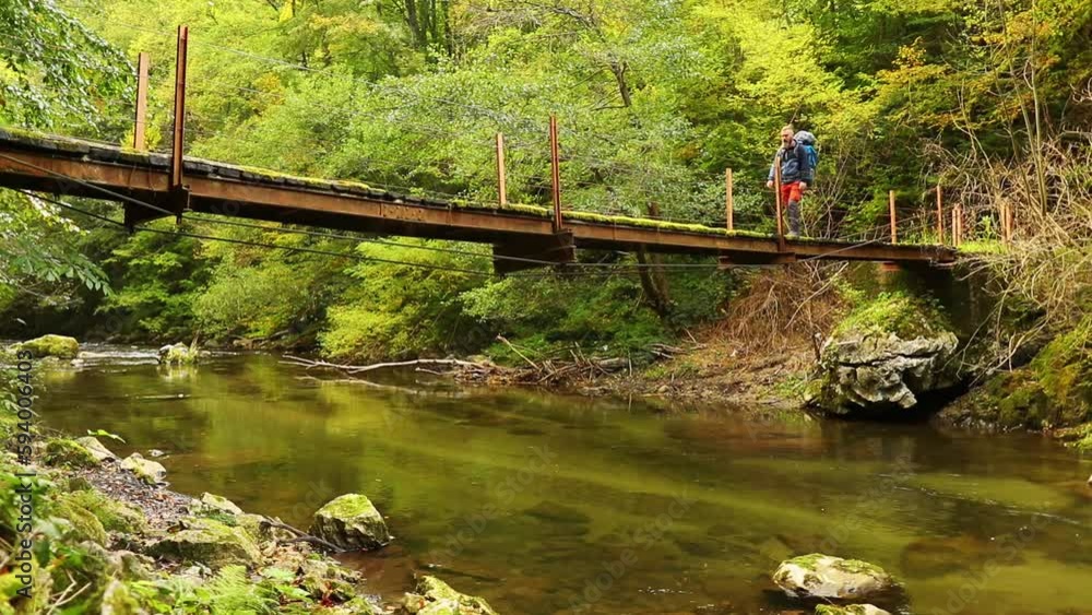 Man with a backpack crossing the river over a wooden bridge Man with a backpack crossing the river over a wooden bridge